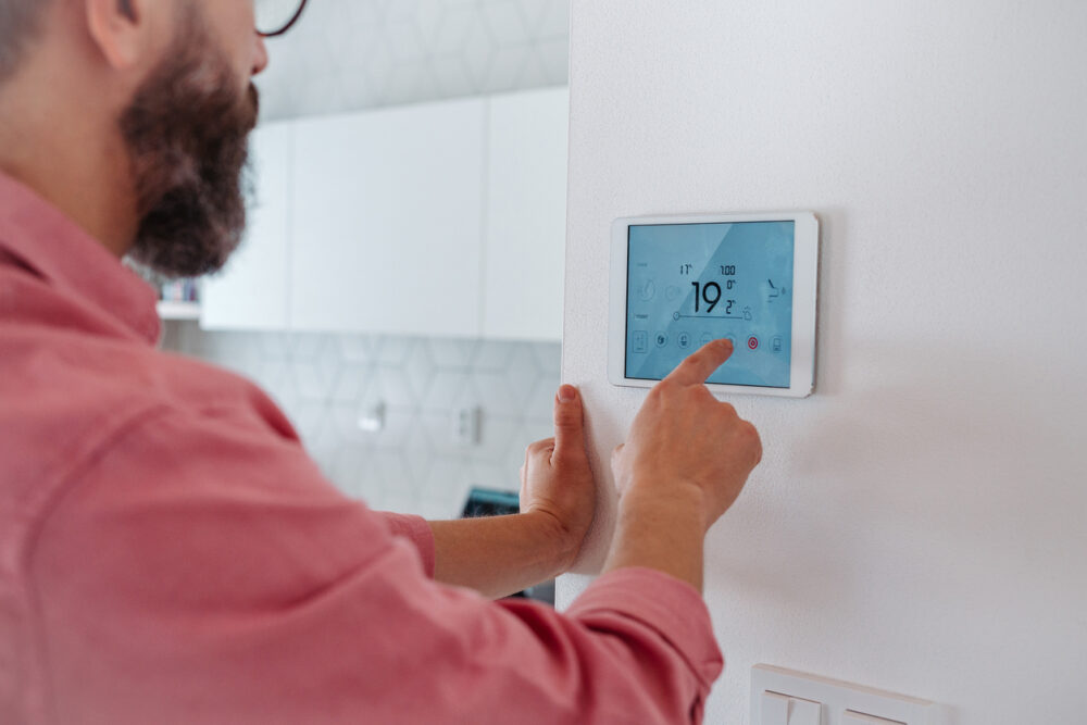 Modern home interior, digital thermostat display, white wall close-up, bright midday light, documentary style photo, one person.