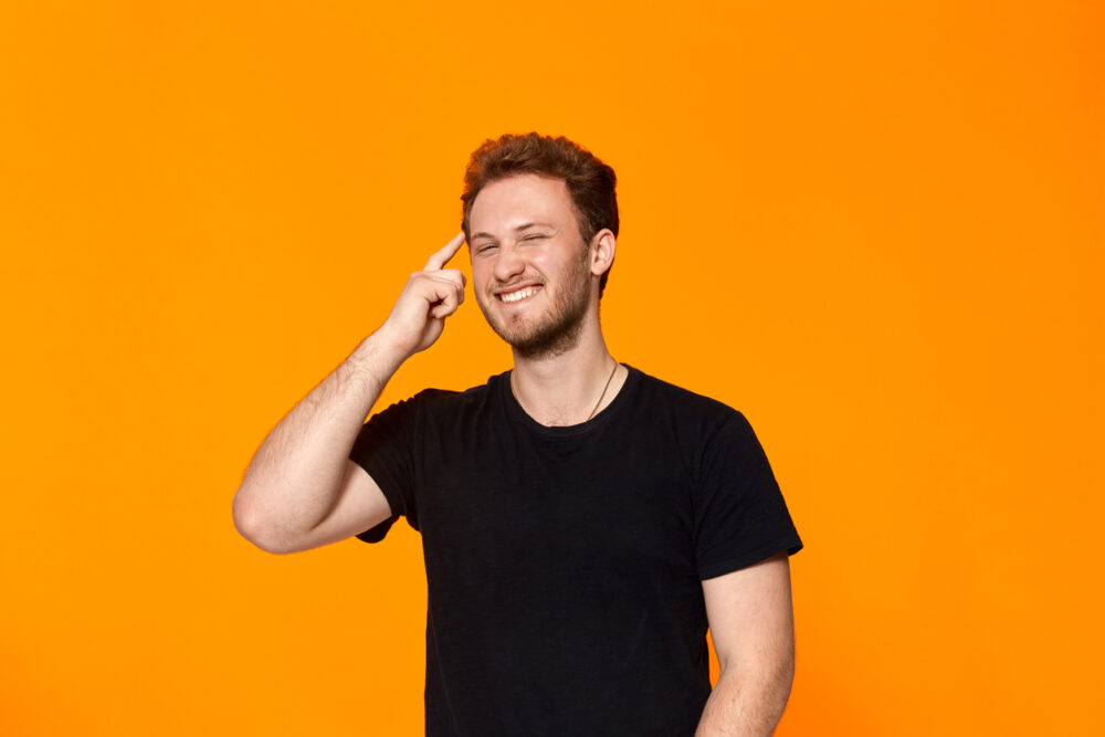 Orange backdrop, man in black t-shirt, half-length portrait, bright lighting, editorial style, one smiling person.