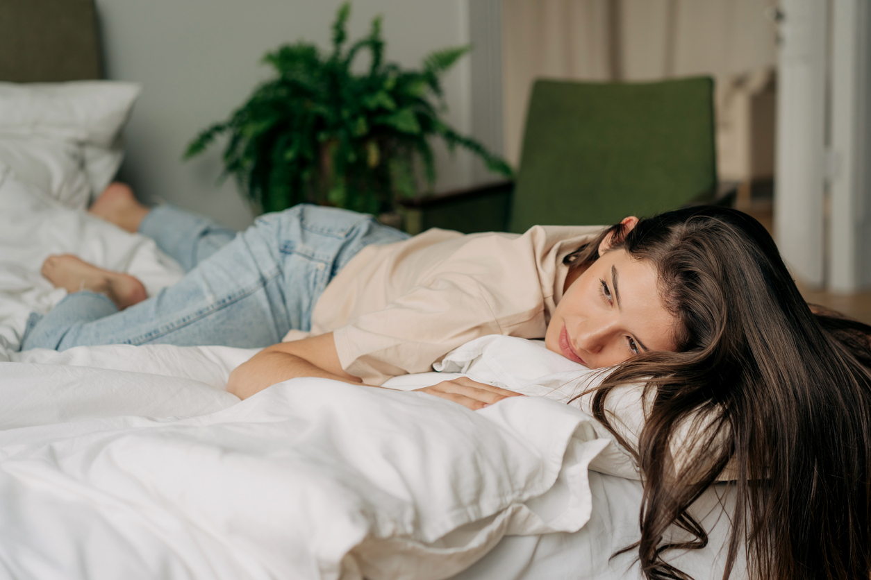 White bedroom, woman face-down on bed, long hair spilled forward, daylight soft, editorial travel photo, one person.