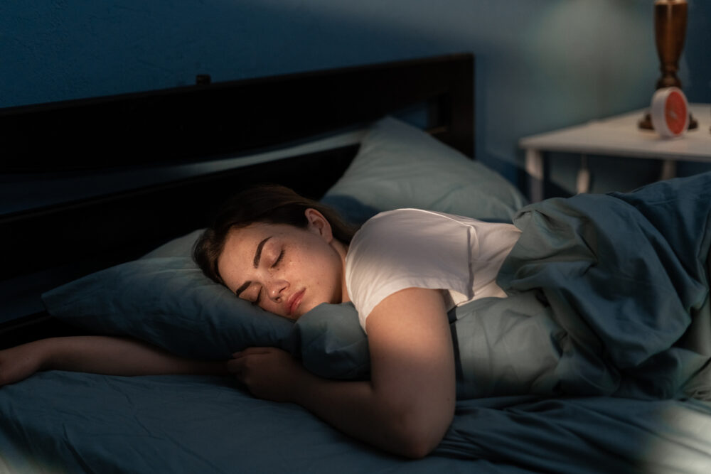Bedroom, dark-haired sleeper with pillow, side view in bed, morning soft light, editorial travel photo, single person.