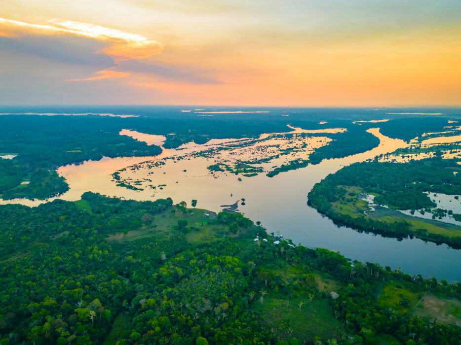 Tropical forest, winding river, aerial composition, sunset orange-yellow glow, editorial travel photo, no people.