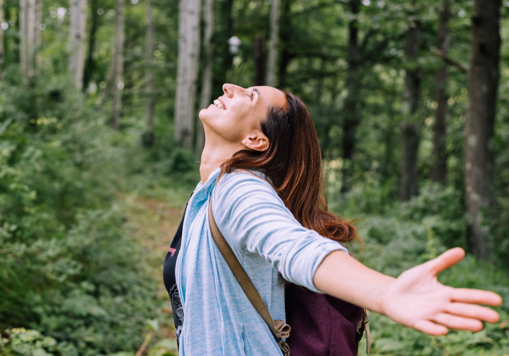 Forest path, joyful hiker, arms wide on trail, soft daylight, editorial travel photo, one person present.