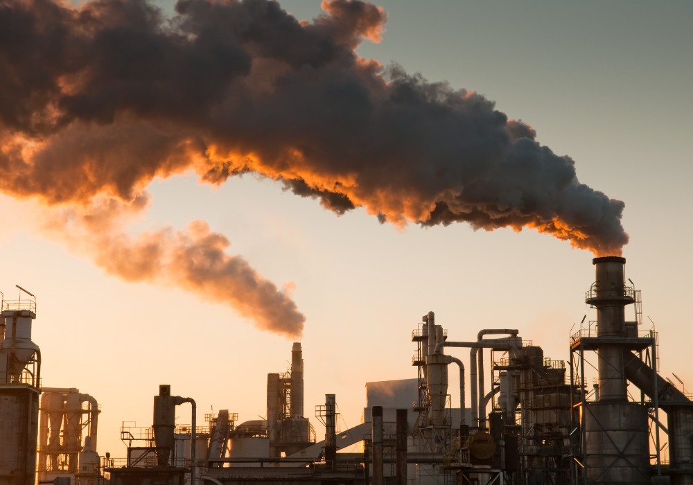 Factory exterior, smokestacks emissions, silhouetted pipes and metalwork, sunset glow, editorial travel photo, no people.