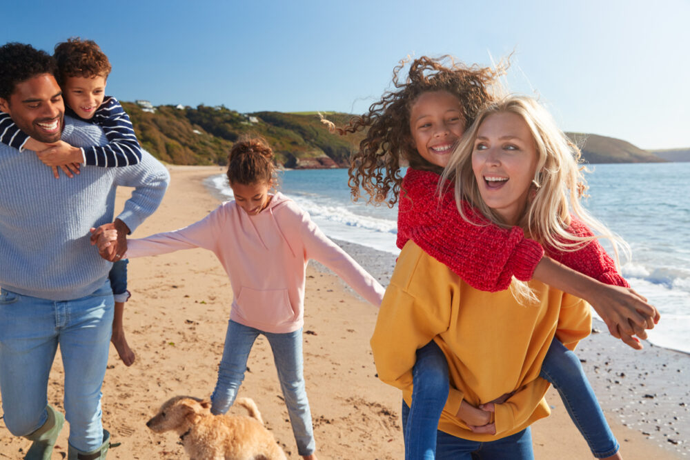 Beach, family with three kids and dog, lively group in foreground, sunny day, editorial travel photo, people.