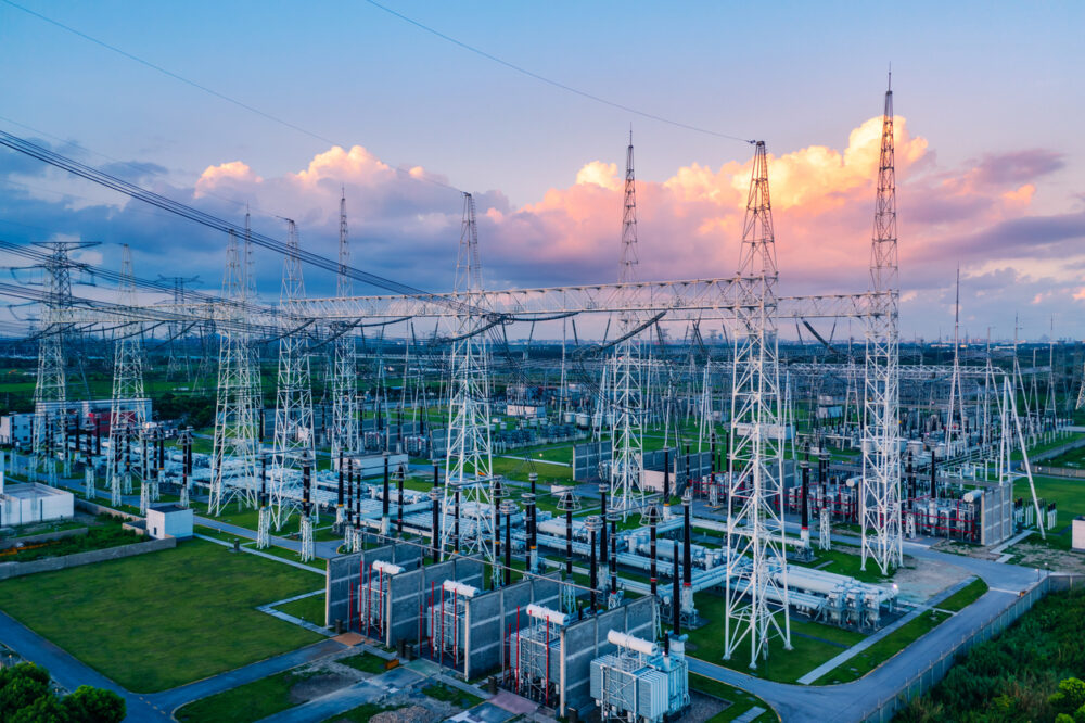 Electrical substation, metal towers and transformers, wide grassy field, sunset clouds, editorial travel photo, no people.