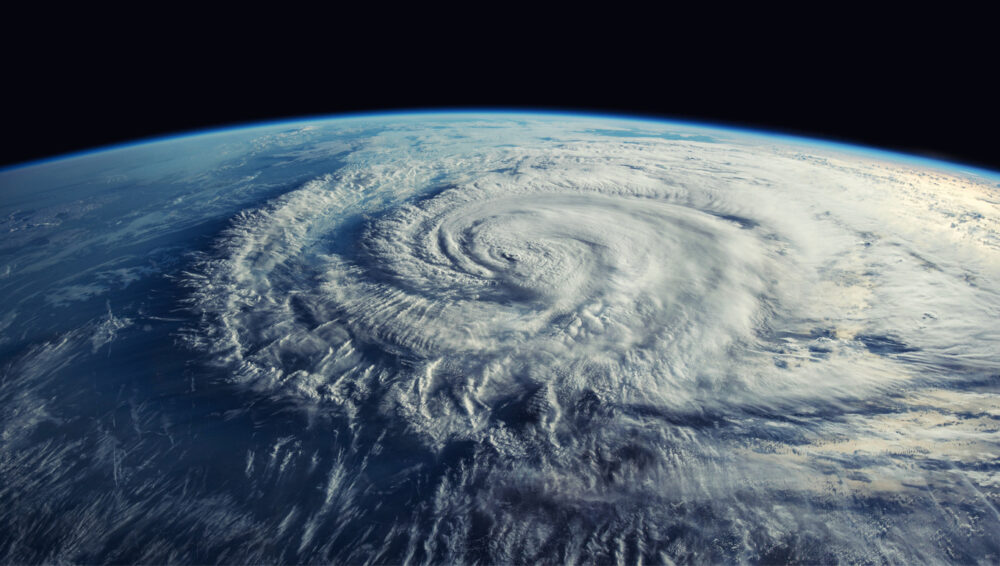Earth from space, hurricane eye center stage, swirling clouds radiate outward, night side visible, documentary style, no people.