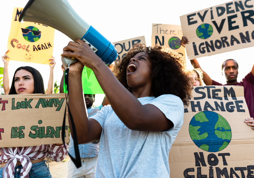 City street, climate protest, woman with megaphone foreground, daytime, documentary style, people holding activist signs.