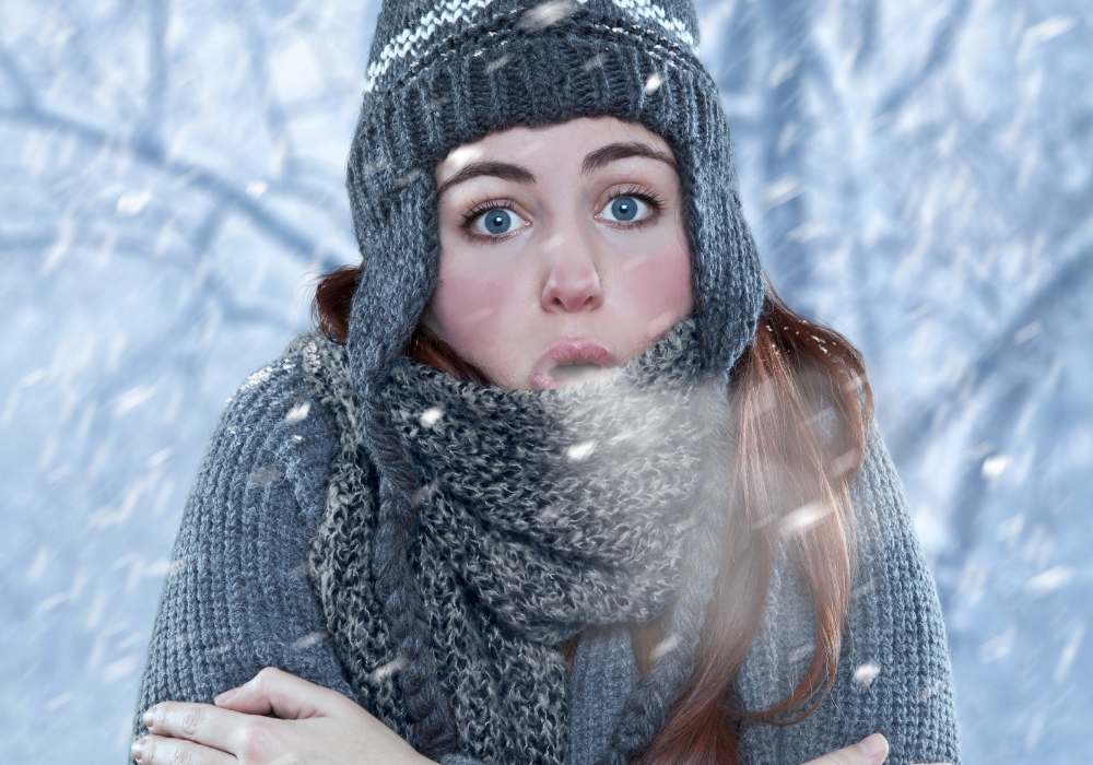 Snowy street, woman hugging herself center frame, winter dusk, visible breath, editorial travel photo, one person.